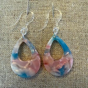 May include: A pair of dangle earrings with a teardrop shape. The earrings are made of a translucent blue, pink, and white material with a swirl pattern. The earrings have a silver hook.