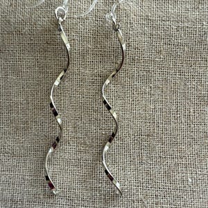May include: A pair of silver-toned, spiral-shaped earrings. The earrings have a twisted design, with a hook at the top for easy wear. The earrings are displayed against a neutral, textured background.