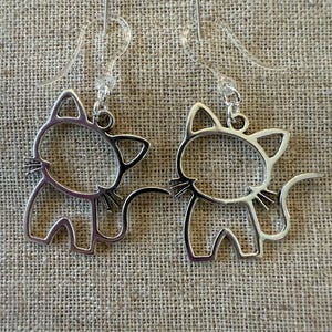May include: A pair of silver cat silhouette earrings with clear plastic hooks.