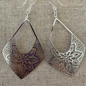 May include: A pair of silver filigree earrings with a diamond shape and a floral design.