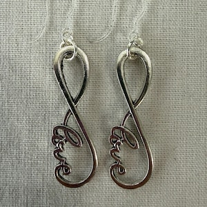 May include: A pair of silver-toned drop earrings. Each earring features an infinity symbol design with the word "Love" in a cursive script at the bottom. The earrings have clear plastic ear wires.