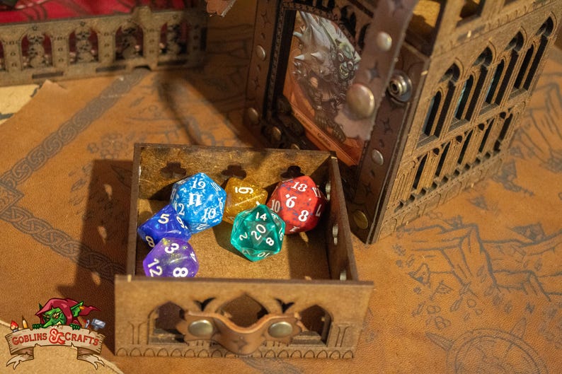 May include: A wooden box with a hinged lid, containing five colorful dice. The dice are blue, green, red, and gold. The box is decorated with a carved design.