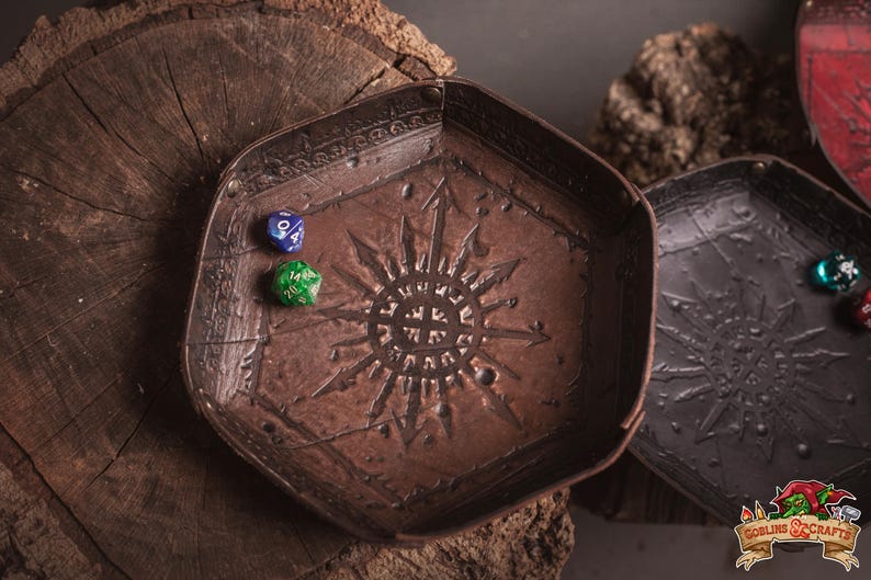 May include: A brown, hexagonal dice tray with a sunburst design and two dice. The tray is made of a textured material and sits on a wooden surface. A second, similar tray is visible.