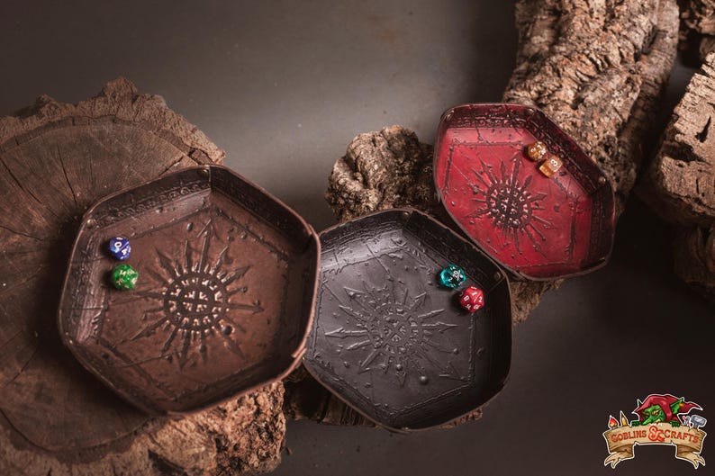 May include: Three hexagonal dice trays in brown, black, and red, each with a sunburst design. Dice of various colors are inside the trays. The trays are displayed on a wooden surface, suitable for tabletop gaming.