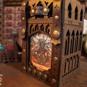 May include: A wooden box with a gothic design, featuring a leather strap and metal accents. The box has a window that displays a fantasy card with a goblin illustration and the text "Creature - Goblin".