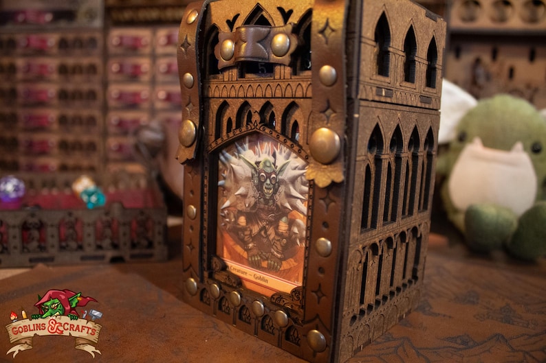 May include: A wooden box with a gothic design, featuring a leather strap and metal accents. The box has a window that displays a fantasy card with a goblin illustration and the text "Creature - Goblin".