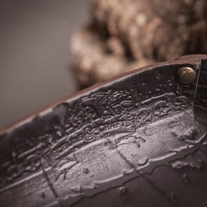 May include: Close-up of a dark brown leather item with embossed details and metal rivets. The item has the text "Goblins & Crafts" and "EDKINS & CRAFTS" embossed on it. The item appears to be part of a larger piece.