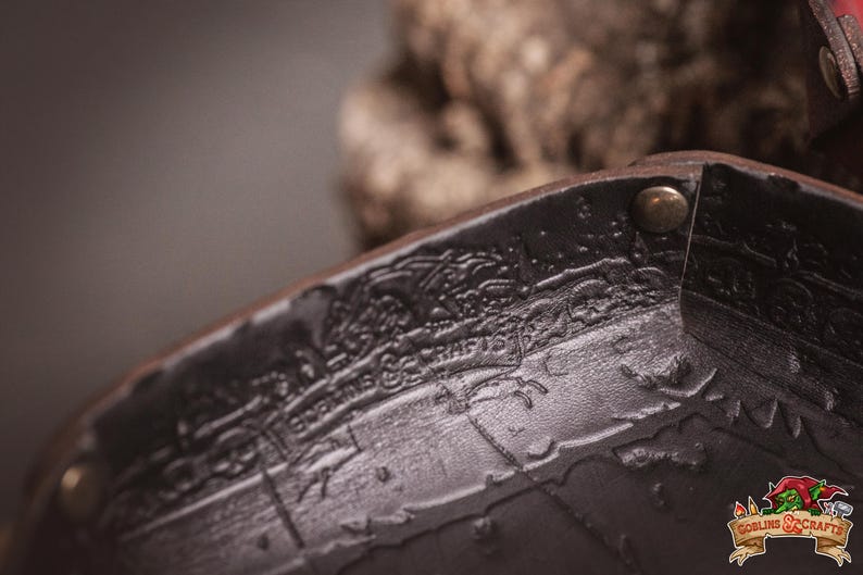 May include: Close-up of a dark brown leather item with embossed details and metal rivets. The item has the text "Goblins & Crafts" and "EDKINS & CRAFTS" embossed on it. The item appears to be part of a larger piece.