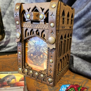 May include: A wooden card box with a gothic design, featuring a leather exterior with metal accents. The box has a clear window that displays a fantasy card with a goblin illustration. The box is labeled "Goblins & Crafts".