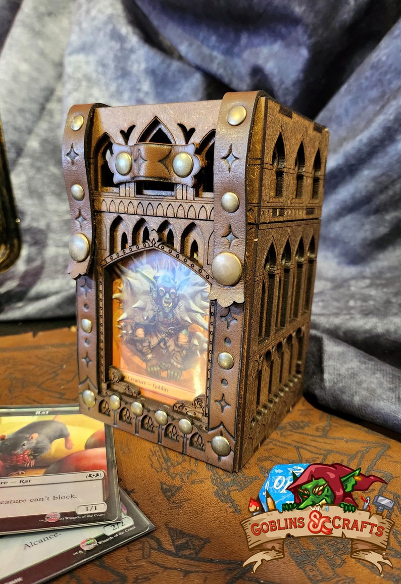 May include: A wooden card box with a gothic design, featuring a leather exterior with metal accents. The box has a clear window that displays a fantasy card with a goblin illustration. The box is labeled "Goblins & Crafts".