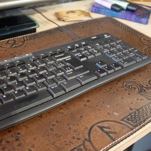Peut inclure: Un clavier d'ordinateur noir repose sur un tapis de bureau en cuir marron avec une bordure décorative. Le tapis a un tapis de souris assorti. La configuration du bureau comprend un écran d'ordinateur et d'autres fournitures de bureau.