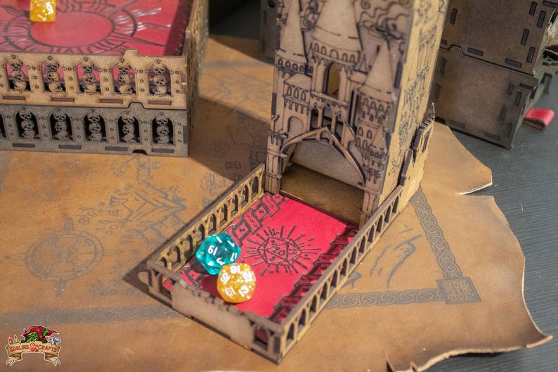 May include: A wooden tower-shaped dice rolling tower with a red felt interior. The tower has a decorative design with a pointed roof and arched windows. There are three dice on the table, one blue, one green, and one gold.