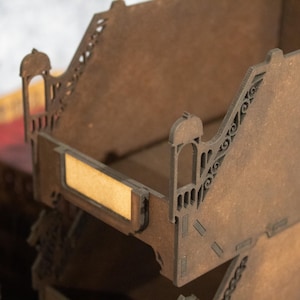 May include: A wooden organiser with multiple compartments, each with a decorative cutout design. The organiser is made of brown wood and has a natural finish. The compartments are stacked on top of each other, and the top compartment has a small label holder.