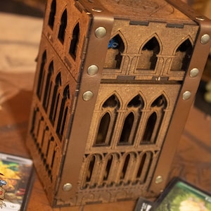 May include: A wooden box with a gothic design, featuring a brown leather trim and metal accents. The box has multiple compartments and is perfect for storing small items.