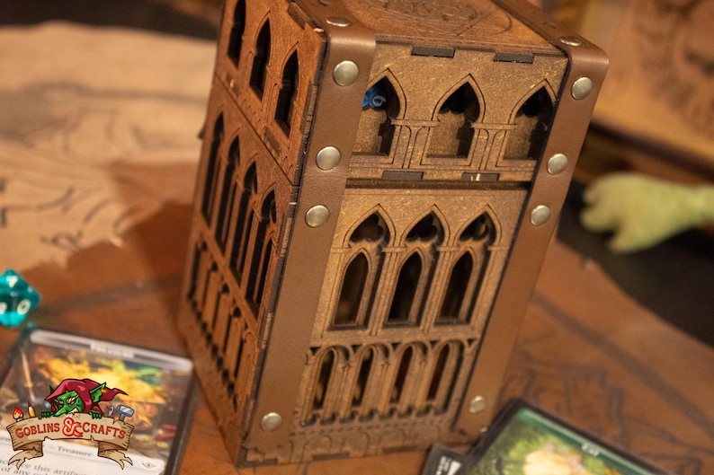 May include: A wooden box with a gothic design, featuring a brown leather trim and metal accents. The box has multiple compartments and is perfect for storing small items.