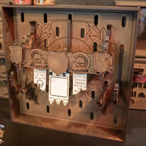 Può includere: Una scatola di legno con un pannello frontale decorativo che presenta uno scudo e stendardi. Gli stendardi hanno il testo "Benvenuti all'Imperatore" e "Adorate l'Imperatore Imperiale Perché Lui è il Vincitore".