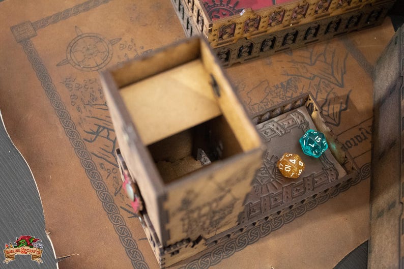 May include: A wooden dice tower with a brown and tan finish. The tower has a decorative design and is open on the top. Two dice are visible inside the tower, one blue and one yellow.