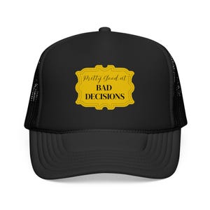May include: Black trucker hat with a curved brim and mesh back. The front features a yellow rectangular emblem with the words "Pretty Good at BAD DECISIONS" in a serif font. A casual accessory.
