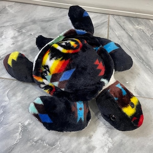 May include: A plush turtle toy with a black, white, blue, red, and yellow geometric pattern on its shell.