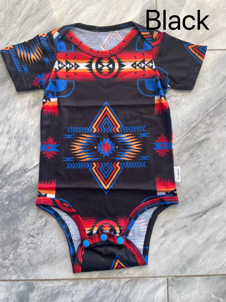 May include: Black baby bodysuit with a colorful geometric pattern in red, blue, orange, and white. The bodysuit has short sleeves and snap closures at the bottom. The word "Black" is printed at the top.