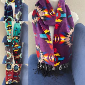 May include: A set of five colorful fleece scarves with a geometric pattern. The scarves are all different colors, including purple, teal, blue, and red. Each scarf has a fringe on the bottom.