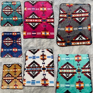 May include: A collection of colorful, patterned blankets. Each blanket features a geometric design with black, white, red, blue, and orange accents. The blankets are rectangular with a black border.