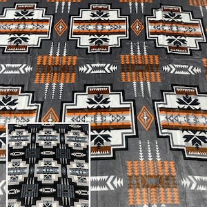 Puede incluir: Una manta gris con un patrón geométrico en blanco, negro y naranja. El diseño presenta formas repetidas y motivos de flechas. Una imagen más pequeña insertada muestra un patrón similar en blanco y negro.