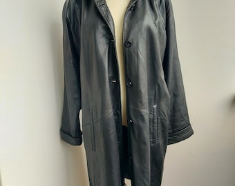 May include: A long, black leather coat with a wide collar and button closure. The coat is displayed on a mannequin and features a tailored fit with pockets and cuffed sleeves. The leather appears to be smooth and has a slight sheen.