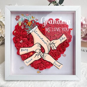 May include: White frame with a red heart made of roses. The heart has five hands reaching into it, with the names "Grandma", "John", "Mary", "Susan", and "David" written on them. The text "Grandma We Love You" is at the top of the frame.