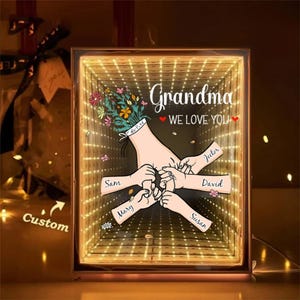 May include: A personalized illuminated box with the words "Grandma WE LOVE YOU." The artwork features a stylized illustration of hands and flowers. Names such as Sam, Mary, Jector, David, and Susan are written on the hands. The word "Custom" is also visible.
