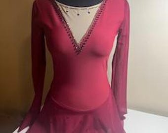 May include: A burgundy figure skating dress with long sleeves and a sheer skirt. The dress has a mesh neckline with rhinestones.