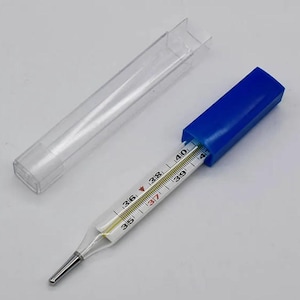 Può includere: Un termometro di vetro con una custodia in plastica blu e una custodia di stoccaggio in plastica trasparente. Il termometro ha una scala in gradi Celsius da 35 a 41.