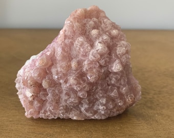 May include: A large, pink, rough-textured crystal cluster with a unique, organic shape. The crystal is composed of many small, pointed crystals that are clustered together.