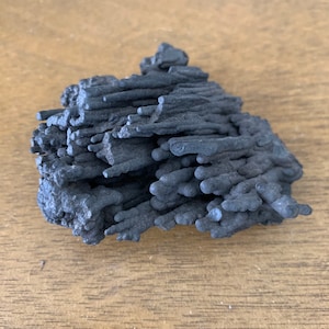 May include: A dark gray, rock-like formation with a textured surface. The rock is made up of many thin, vertical, and slightly curved lines.