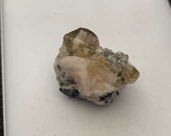 May include: A cluster of light brown and clear crystals on a matrix of pink and gray rock.