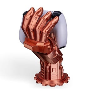May include: A copper-colored robotic hand sculpture with intricate mechanical details, holding a white object. The hand is mounted on a base with a gear-like design. The sculpture has a futuristic, industrial aesthetic.