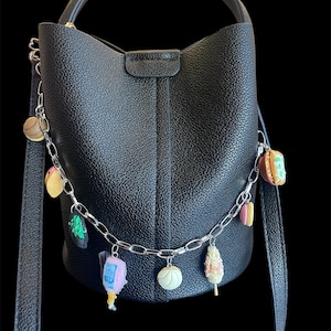 May include: Black bucket bag with a silver chain and food-themed charms. The bag has a top handle and a long shoulder strap. Charms include a taco, ice cream, and a corn dog.
