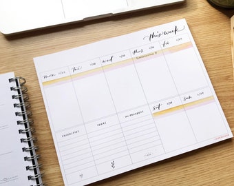 May include: A weekly planner with a watercolor background in shades of yellow and pink. The planner has sections for each day of the week, with spaces for "priorities", "ideas", and "in progress". The text "this week" is written at the top of the planner.