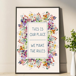 May include: Framed art print featuring a floral wreath design with butterflies. The artwork has a cream background and a rectangular text box with the words "THIS IS OUR PLACE WE MAKE THE RULES". The frame is black.