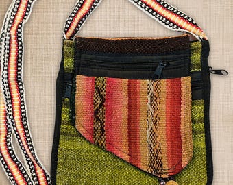 May include: A crossbody bag featuring a lime green woven fabric base with a black zipper closure. An attached front pocket displays vertical stripes in shades of orange, red, and yellow. The long shoulder strap has a matching striped pattern.