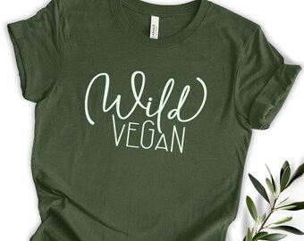 Op de afbeelding: Een olijfgroen t-shirt met de woorden "Wild Vegan" in witte letters. Het shirt is gemaakt van een zacht materiaal en heeft korte mouwen. De tekst is in een handschriftstijl.