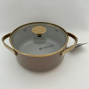 May include: A brown cooking pot with a glass lid and gold-colored accents. The pot has two handles and a gold-colored knob on the lid. The pot is labeled "masterclass".