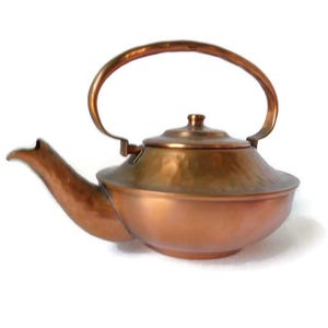 May include: A copper teapot with a hammered finish and a curved handle. The teapot has a lid and a spout.