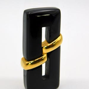 May include: A rectangular black brooch with a gold-colored band encircling the center. The brooch has a glossy finish and a minimalist design, suitable for various outfits.