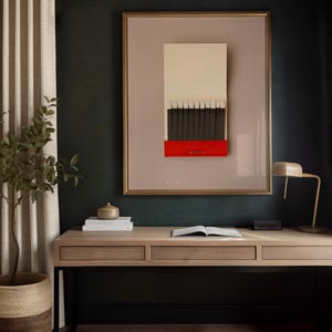 Könnte beinhalten: Ein gerahmtes Kunstwerk, das ein Streichholzheft mit dunklen Streichhölzern, einem roten Sockel und einer cremefarbenen Oberseite darstellt. Das Kunstwerk hängt über einem Holzschreibtisch mit einer Lampe, Büchern und einer kleinen Pflanze. Der Raum hat eine dunkelgrüne Wand und beige Vorhänge.