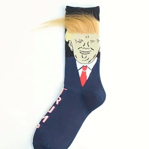 May include: A pair of blue socks featuring a cartoon image of a man with blonde hair wearing a suit and red tie. The socks have the word "TRUMP" written on them.