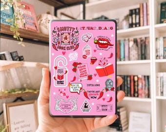 Puede incluir: Una funda rosa para lector de libros electrónicos con pegatinas. Incluye textos como "Smutty Book Club", "Hot & Spicy" y "Do Not Disturb". El diseño presenta corazones, chiles y gráficos relacionados con libros.
