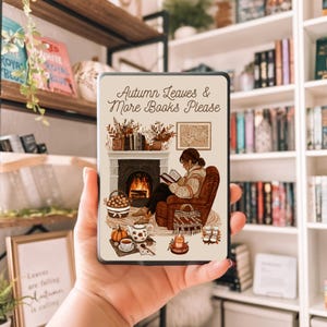 May include: A rectangular phone case featuring an illustration of a cozy autumn scene. The image depicts a person reading by a fireplace, with text that reads "Autumn Leaves & More Books Please." The case has a cream-colored background with fall-themed imagery.
