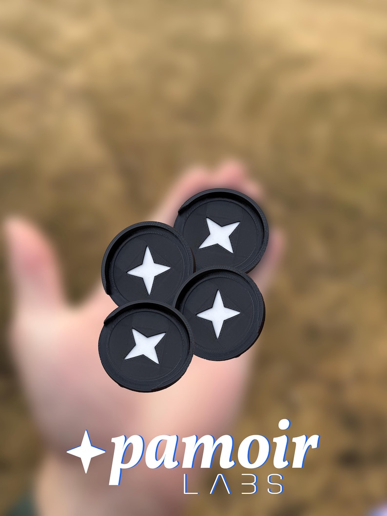 May include: Four black lens caps with a white star design. The lens caps are stacked on top of each other and are being held in a hand. The background is blurred and out of focus. The text "pamoir LABS" is visible in the lower part of the image.