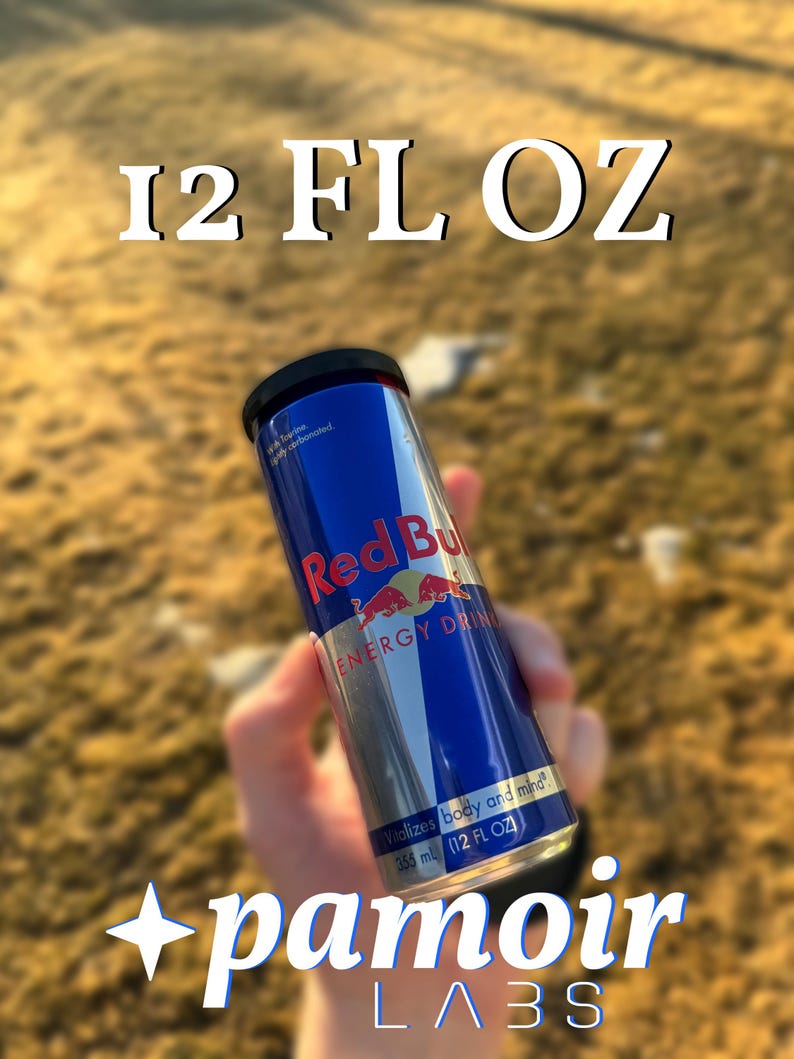 May include: A blue and silver Red Bull energy drink can with the text "12 FL OZ" at the top. The can has the Red Bull logo and text, and the bottom of the can reads "355 ml (12 FL OZ)". The image also includes the text "pamoir LABS".